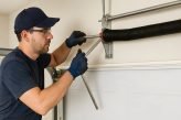 Professional garage door technician repairing torsion spring with tools, maintenance worker adjusting overhead mechanism, handyman service concept, industrial repair engineering, home improvement safe